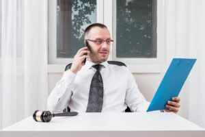 A man wearing a suit and holding a blue clipboard talking on a mobile device