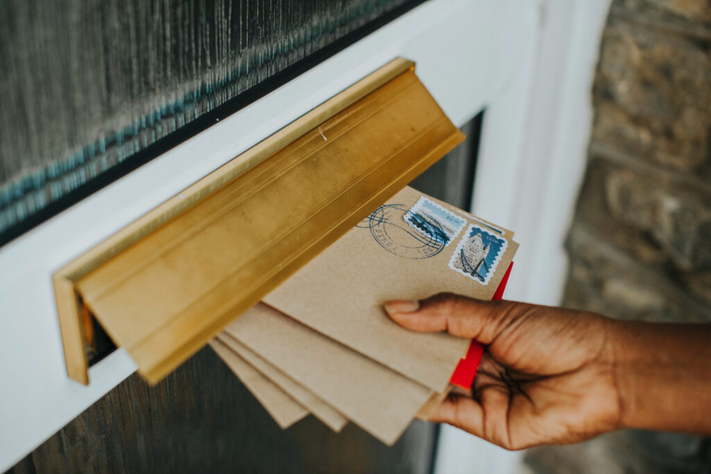 Hand placing certified mail envelopes through a brass mail slot on a residential door