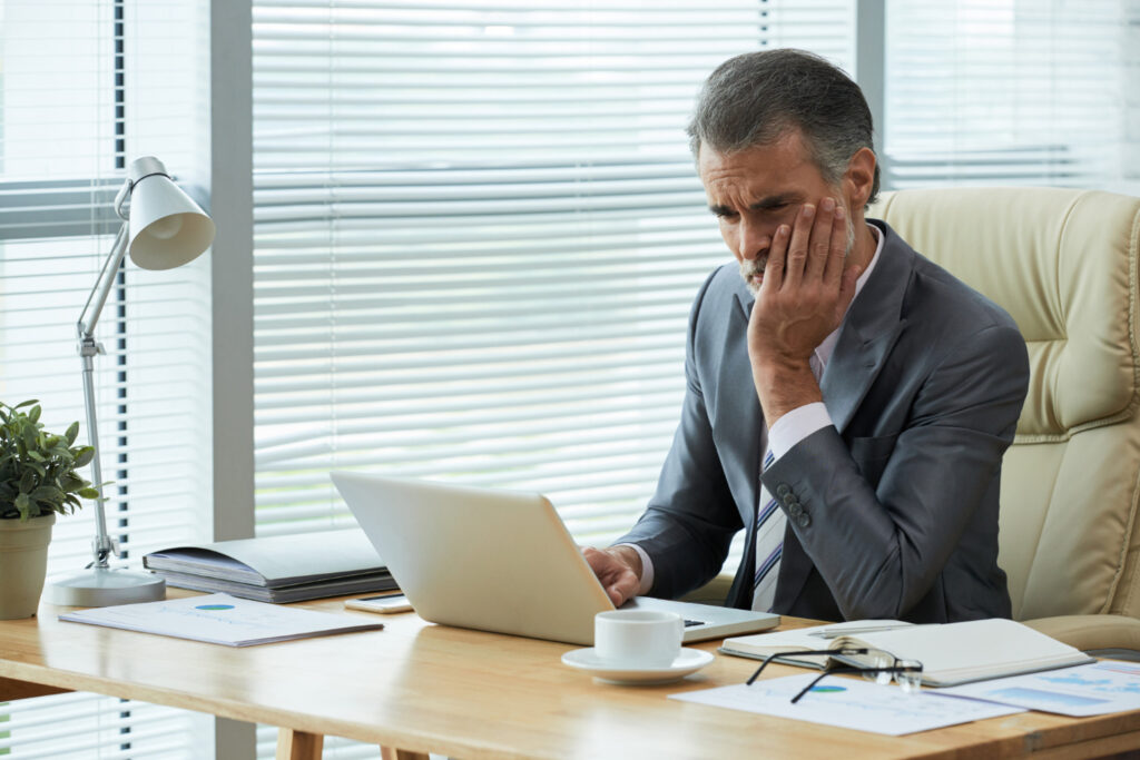 Concerned businessman in a suit looking at his laptop in a modern office setting