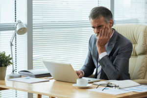 Concerned businessman in a suit looking at his laptop in a modern office setting